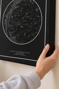 Close-up of a black star map showing labelled constellations, the Milky Way and the coordinates of the night